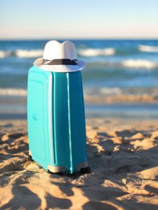Blue suitcase & white hat on the beach